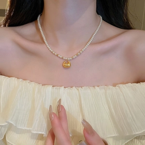 Close-up of a pearl necklace with a golden lucky bag pendant worn by a model