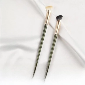Detailed sickle-shaped nose shadow brush with dark green handle and gold metal ferrule