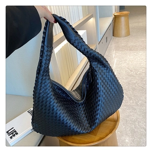 Detail shot of a black woven leather tote bag resting on a round wooden table indoors