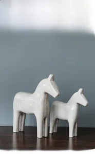 Detail view of two minimalist wooden horse sculptures with distressed white texture finish