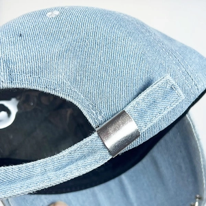 Detail einer hellblauen Jeans-Baseballkappe mit verstellbarer Metallschnalle und Nähten