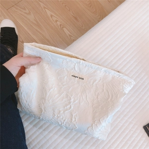 Close-up of white embossed floral texture and logo label on the canvas clutch bag