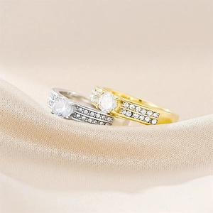 Close-up of gold and silver zircon rings on beige satin base showing luxury textures