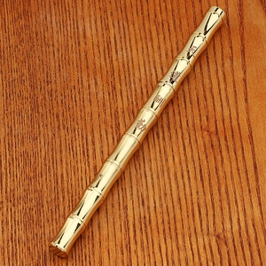 Detailed close-up of bamboo-shaped brass pen with Chinese engraving on wooden background