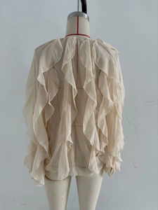Detail of beige layered ruffle blouse featuring sheer fabric and tie-front bow design