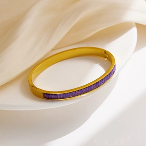 Detailed macro view of a gold-plated bangle with rectangular purple gemstones on white ceramic