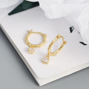 Macro detail of gold irregular wavy hoop earrings with square clear zircon pendants