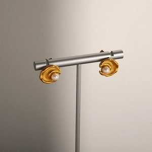 Close-up of irregular brushed gold earrings featuring a central white pearl inlay