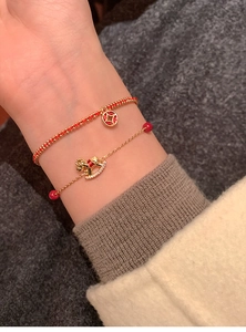 Detailed close-up of 18k gold-plated pony bracelet with red beads on a soft knit sleeve
