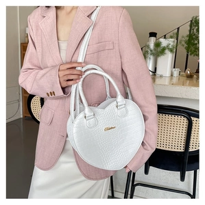 Vue détaillée d'un sac à main blanc en forme de cœur avec motif crocodile porté