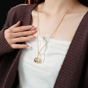 Detail showing a sleek gold ball pendant necklace worn with an elegant sweater