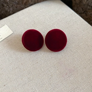 Close-up of red velvet round stud earrings on a beige textured fabric background