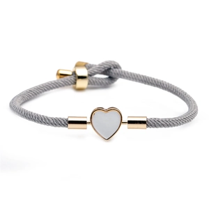Gray woven cord bracelet featuring a gold-edged heart pendant on a white background