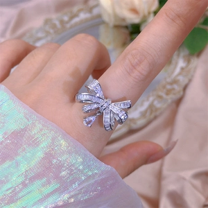 Macro detail of silver bow ring with zircon pavé and teardrop crystal on silk fabric