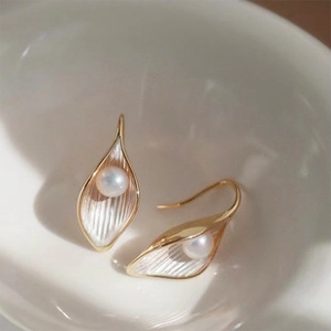 Vista macro di orecchini a calla dorati con petali testurizzati e perle bianche
