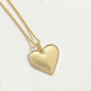 Macro view of a gold heart pendant with fingerprint texture and white zircon micro-paving