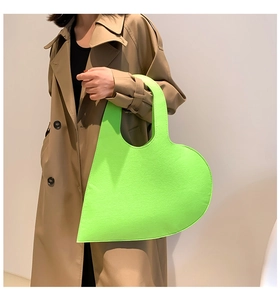 Detail of neon green heart-shaped felt handbag held by model in stylish trench coat