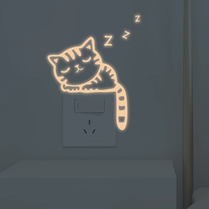 Luminous sleeping cat wall sticker glowing with warm light above a white power socket