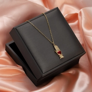 Close-up of golden palm pendant with red heart gemstone on pink silk background