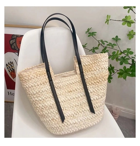 Détail d'un sac cabas tissé à la main avec anses en cuir noir posé sur une chaise blanche