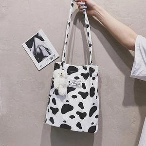 Detail of cow print canvas tote bag featuring black woven label and plush bear charm