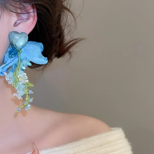 Detail of blue heart floral tassel earring with fabric petals and beads on model
