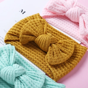 Three waffle knit baby headbands with large bows in pink, mustard yellow, and mint green