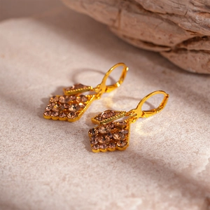 Macro shot of geometric gold earrings with champagne rhinestones on a natural stone background