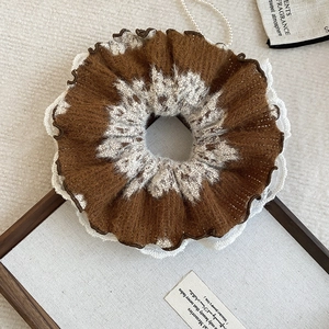 Close-up of brown and white knit scrunchie with delicate lace trim on rustic wooden canvas