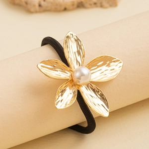 Minimalist gold metal flower hair tie with pearl center and textured petals on beige display