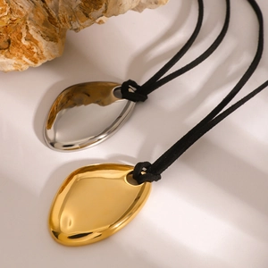 Gold and silver irregular oval metal pendants on black cord necklaces over a beige stone background
