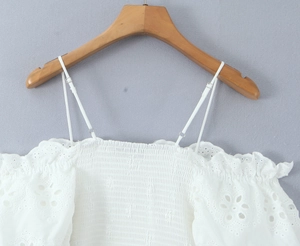 Detalle de top blanco con hombros descubiertos, cuerpo elástico y bordado de encaje