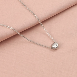 Detailed view of silver shell pendant on a fine chain over soft pink fabric background