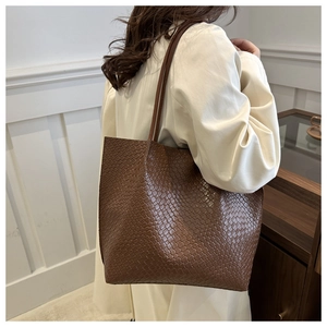 Detail view of large brown tote bag with woven texture on a model's shoulder