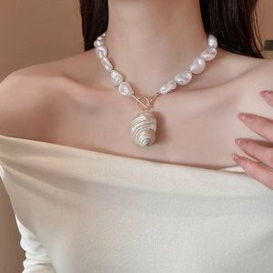 Detail of baroque pearl necklace with a large conch shell pendant and golden T-bar clasp