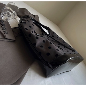 Close-up of dark grey polka dot canvas tote with black patent leather trim on a blazer