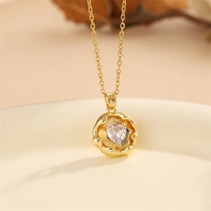 Close-up of golden heart pendant necklace with clear zircon stone on ceramic plate