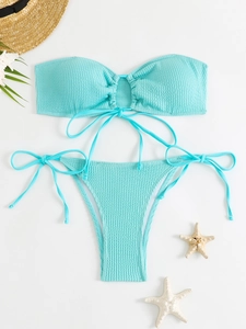 Flat lay of light blue textured bikini with bandeau top and side-tie bottoms on beach props