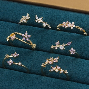 Détail de bagues dorées fleurs et papillons avec zircons roses sur fond velours