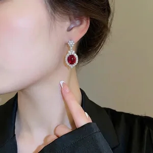Elegant oval Ancora red ruby earrings with silver diamond halo on a female model