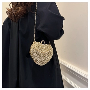 Close-up of heart-shaped gold rhinestone evening bag with chain strap on a black coat