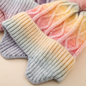 Macro detail of rainbow gradient cable-knit texture and soft faux fur pom-pom on winter hat
