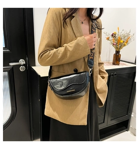 Close-up of black glossy leather saddle bag featuring a wide logo strap on khaki blazer