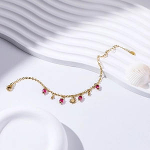 Close-up of gold-plated sun charm bracelet with pink beads and shell background