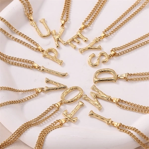 Macro view of textured gold letter pendants with rustic bark finish and double layer chain