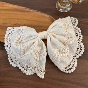 Detailed view of cream lace bow hair clip with intricate embroidery on a wooden tray