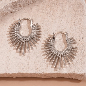 Detail of silver sunburst earrings with pointed rays on a textured beige stone background
