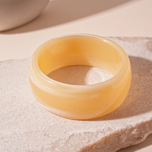 Detail of cream yellow striped acrylic bangle resting on a textured beige natural stone