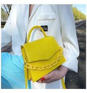 Detail view of bright yellow leather handbag with chunky chain handle and square structure