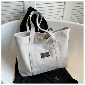 Detail of minimalist beige canvas tote bag with black label on a white chair setting